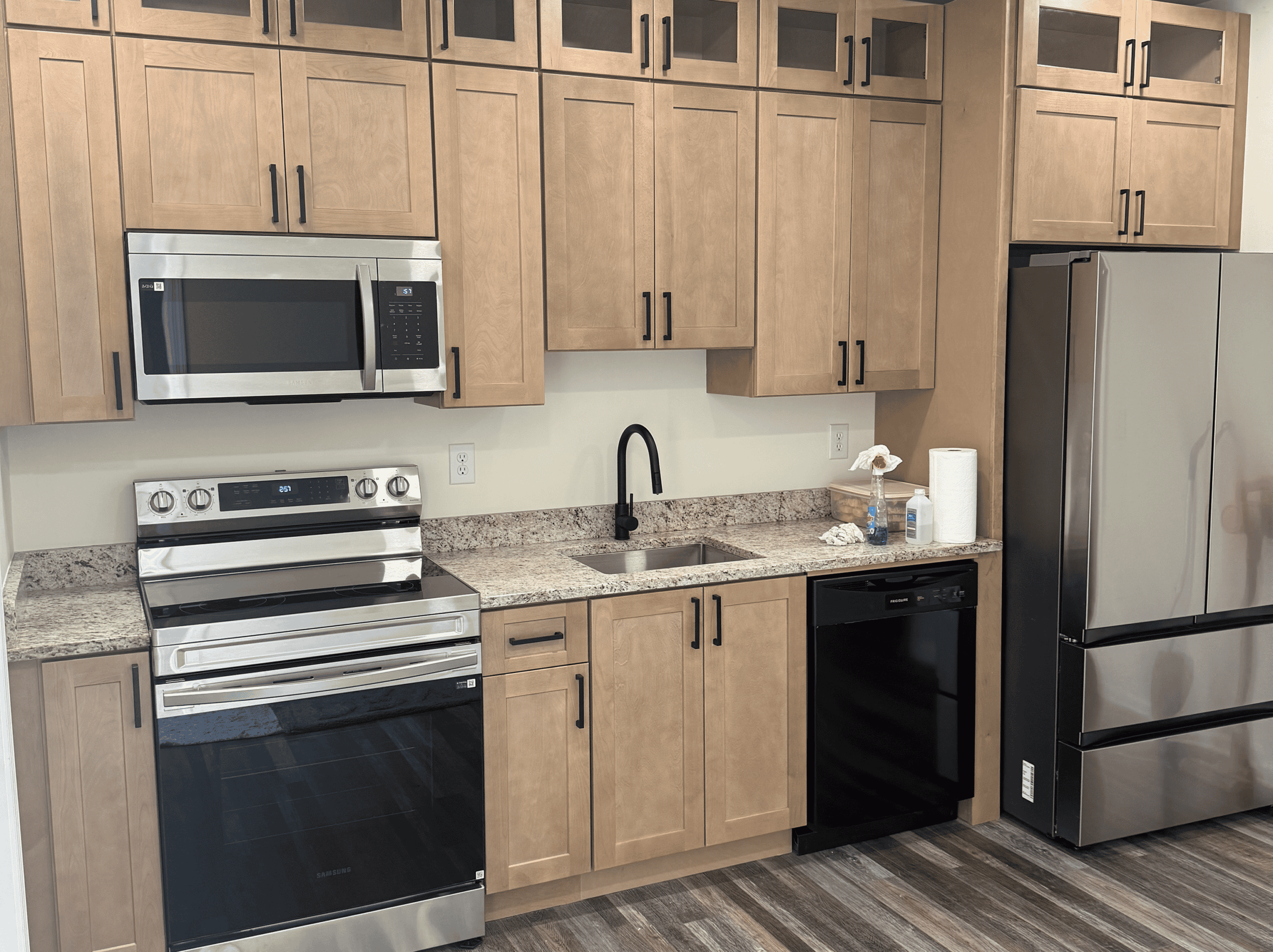 Modern kitchen with wooden cabinets and stainless steel appliances Kitchen with wooden cabinets, stainless steel refrigerator, oven, microwave, and black dishwasher.