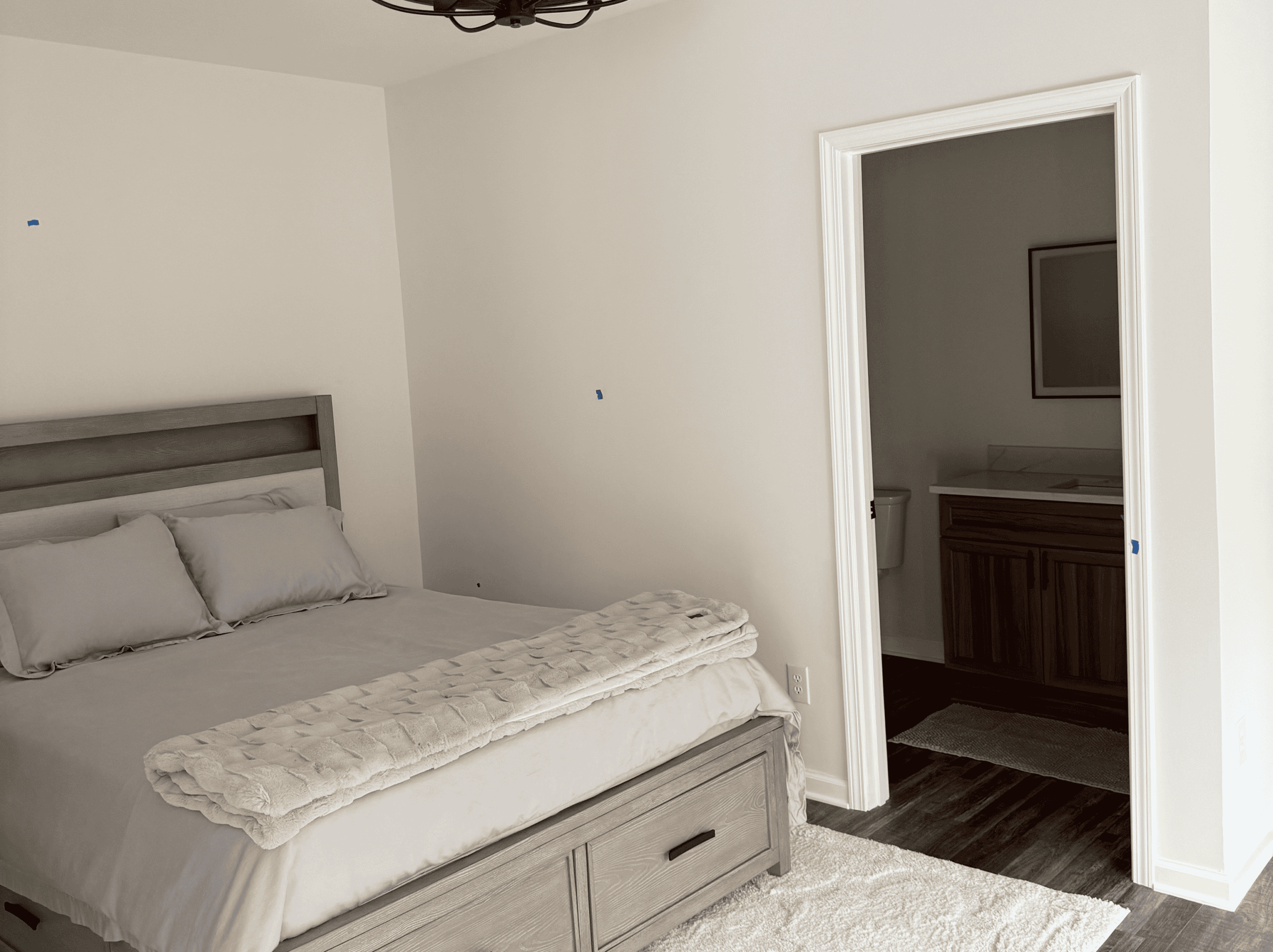Bedroom with beige walls, cozy bed, and connected bathroom with wooden vanity.