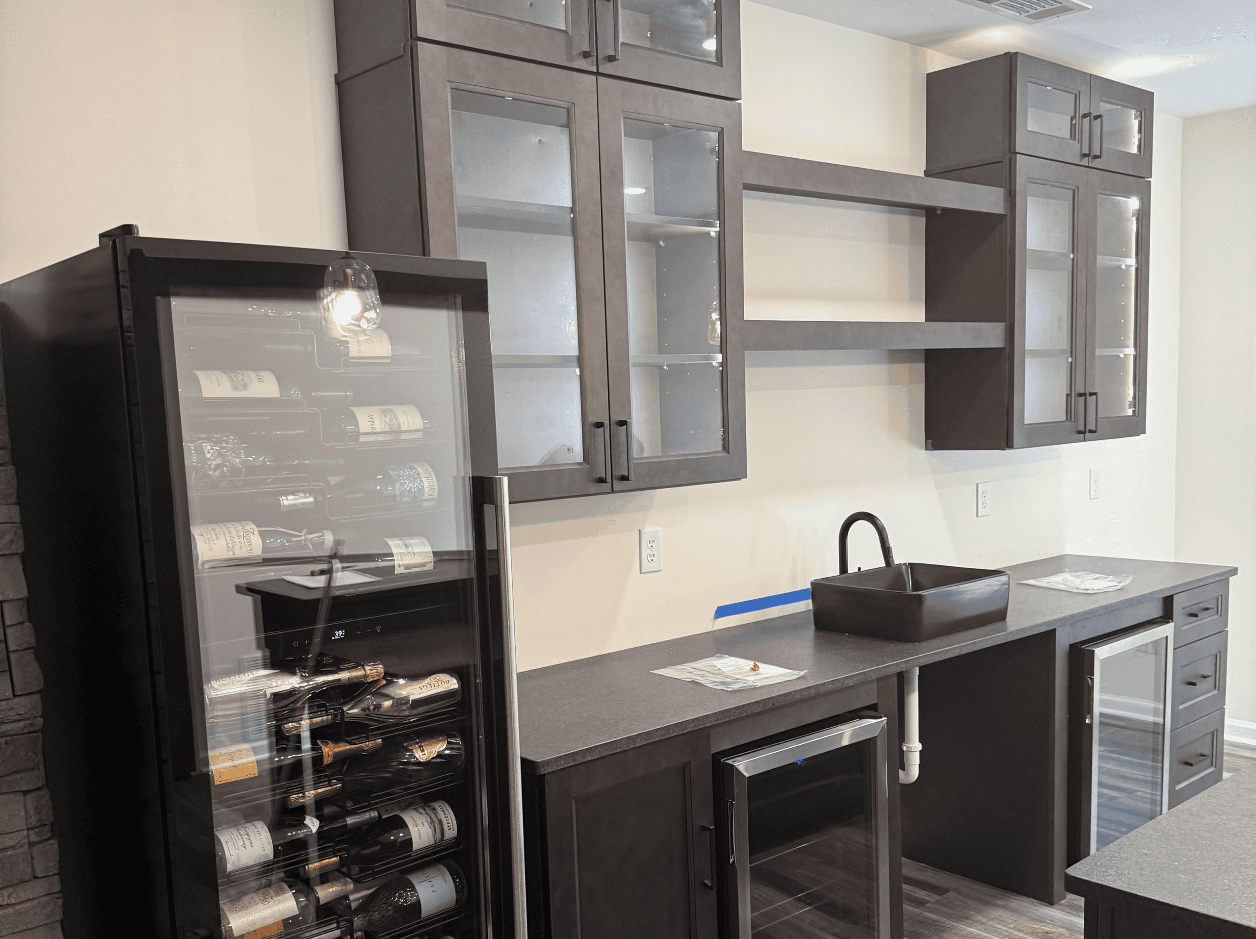 Modern kitchen with dark cabinetry and wine fridge. Kitchen cabinetry with wine fridge and black sink.
