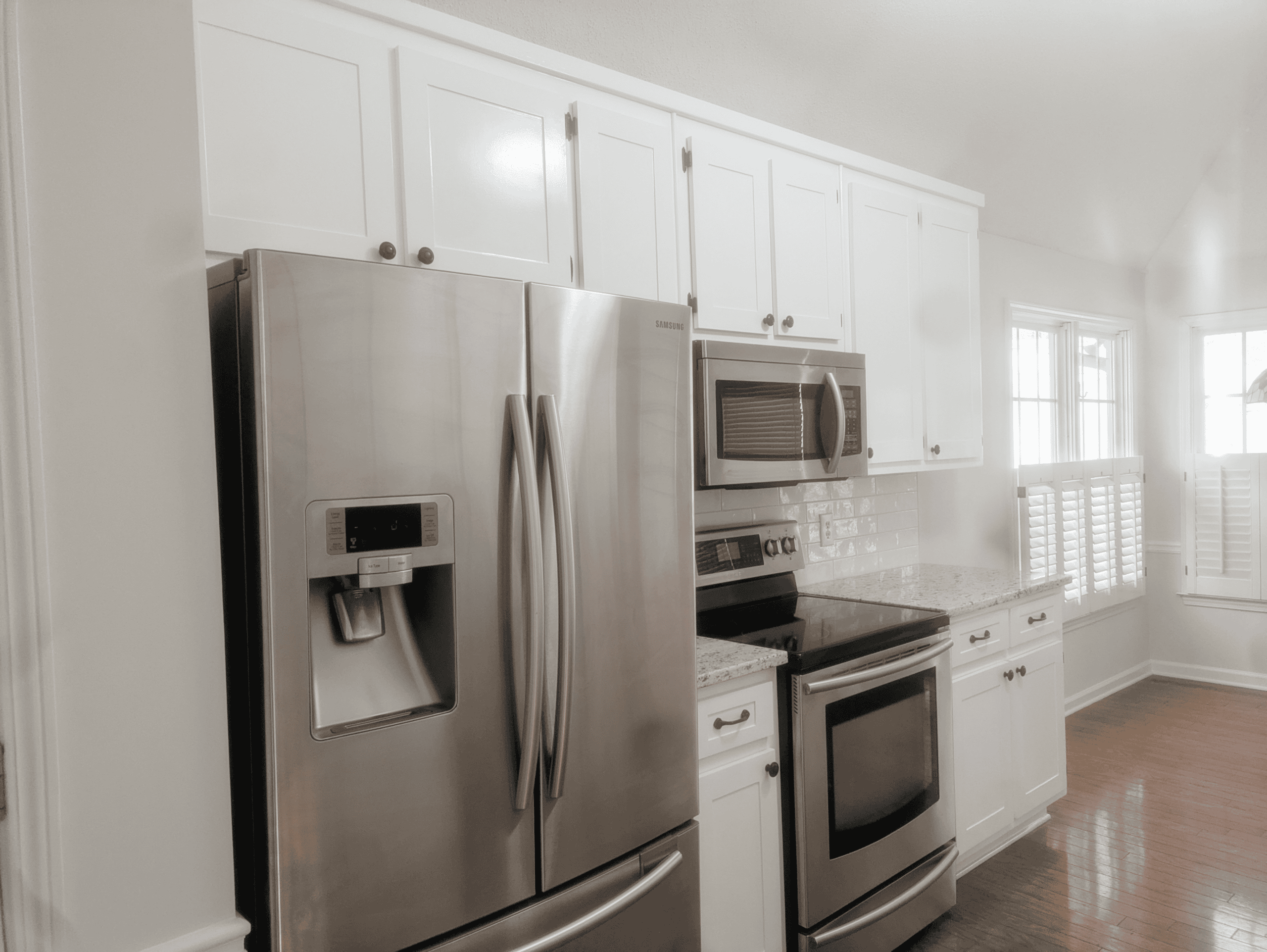 Modern stainless steel kitchen appliances with white cabinetry. Stainless steel refrigerator, microwave, and oven in a bright, clean kitchen.