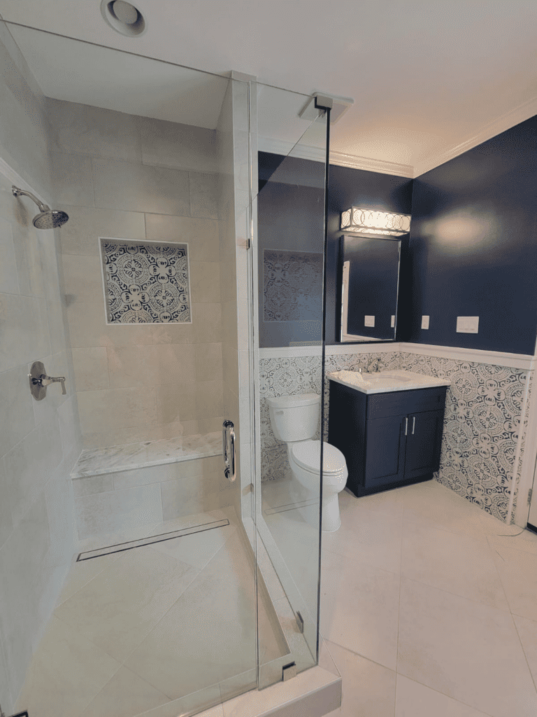 Modern bathroom with walk-in shower, glass enclosure, and navy blue vanity with decorative wall tile.