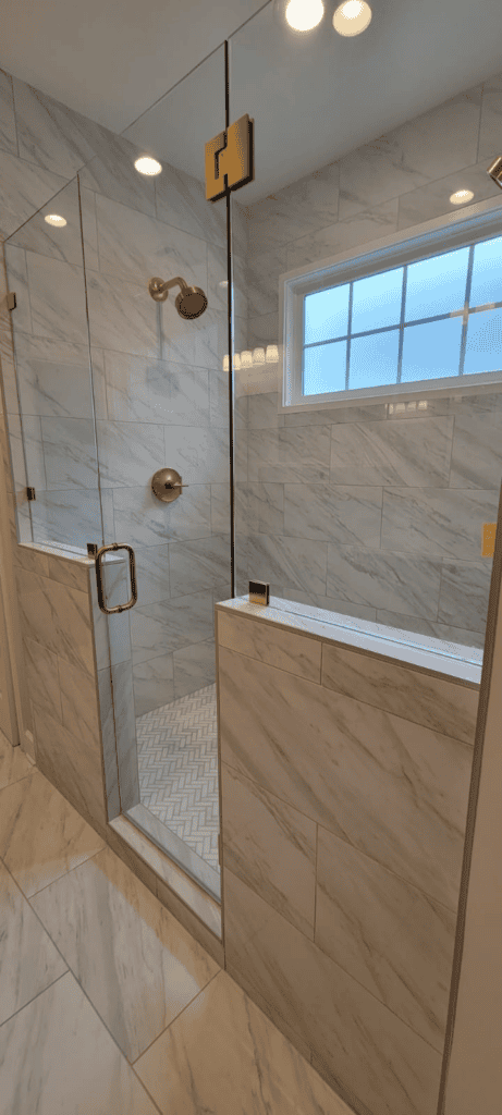 Elegant glass shower with gold fixtures and marble walls.