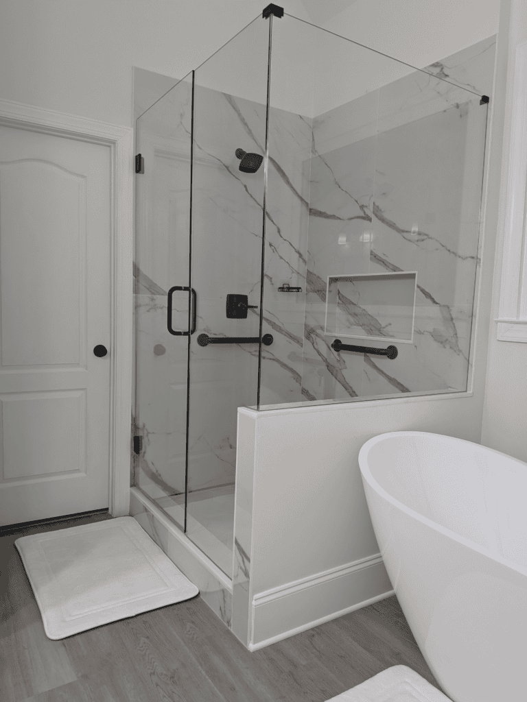 Glass shower with black hardware and marble walls.