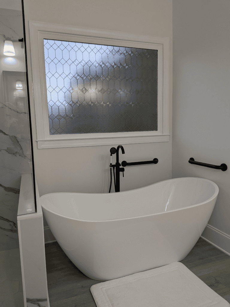 Freestanding white bathtub with black fixtures in a contemporary bathroom setting.